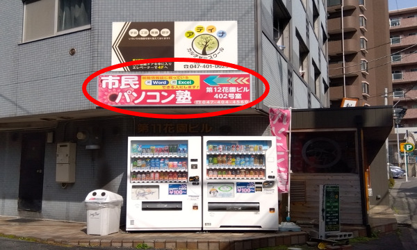 すぐに自販機2台と市民パソコン塾の看板があるビルが見えます（ハイジ西船橋駅前店が入居している第11花園ビルです）